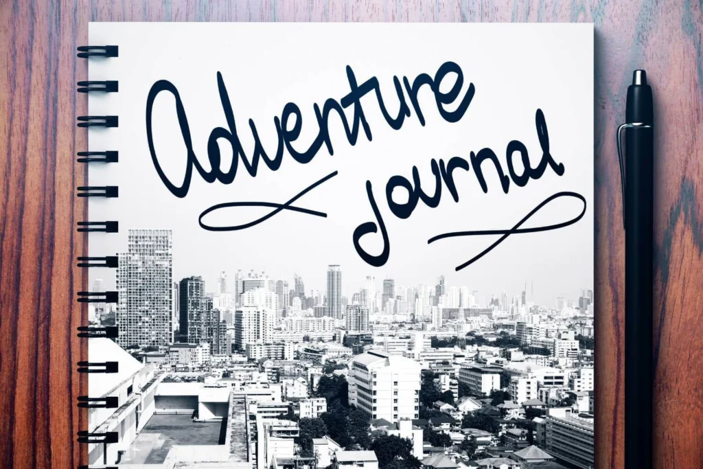 A woman sitting cross-legged on her bed in a cosy sweater, writing in a blank journal with a pencil, capturing solo travel memories at home.