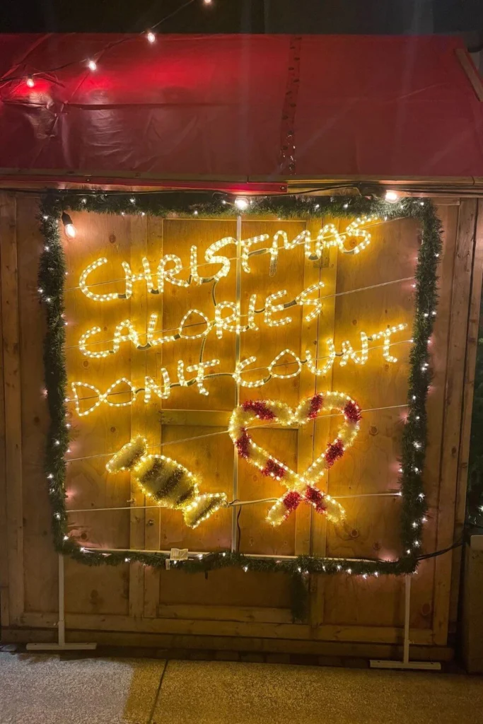 A festive Christmas market light-up sign reading Christmas Calories Don’t Count, surrounded by holiday garlands and warm string lights.