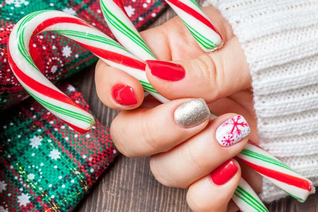 Close-up of a woman’s festive Christmas manicure with red polish, silver glitter and snowflake nail art while holding candy canes.