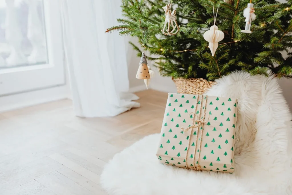Wrapped Christmas present with green tree pattern paper placed under a simple scandi-style tree with neutral ornaments and a faux fur rug.