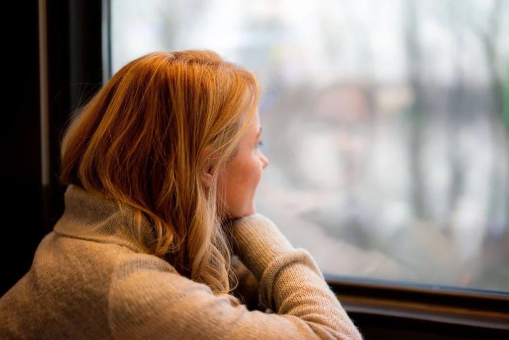 Solo female traveler leaning against a train window, reflecting and daydreaming about future adventures.