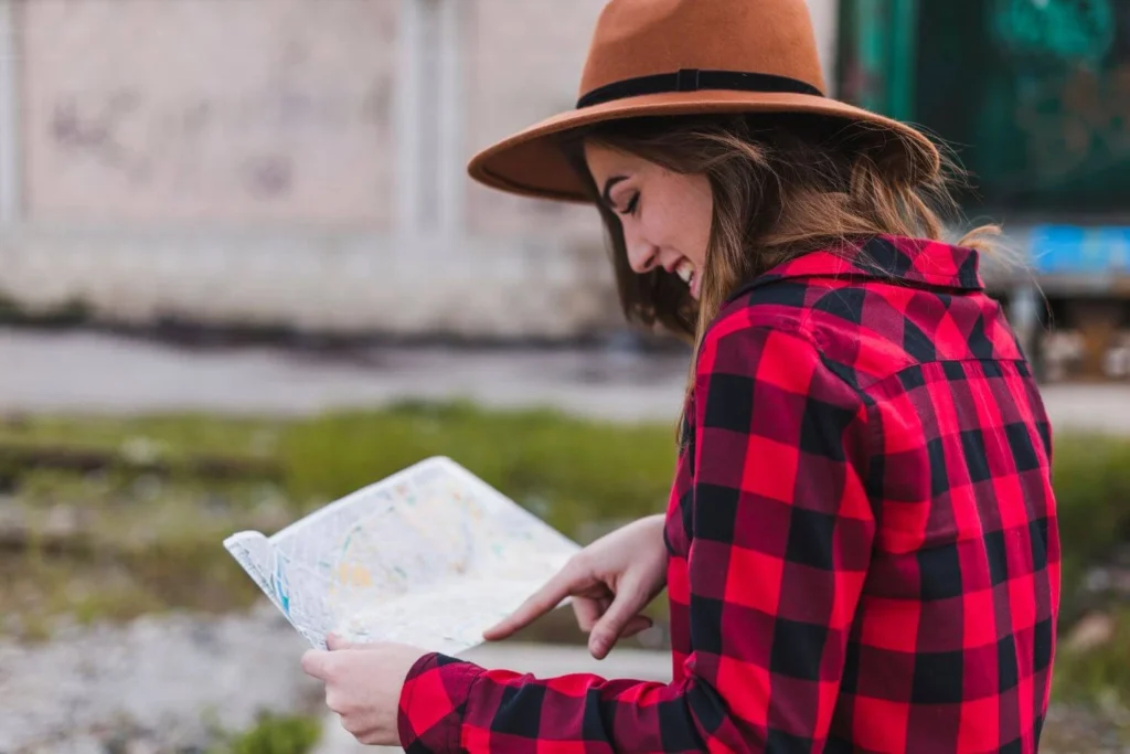 A solo female traveller holding a map while overlooking a mountain landscape, checking her route and staying aware of her surroundings.