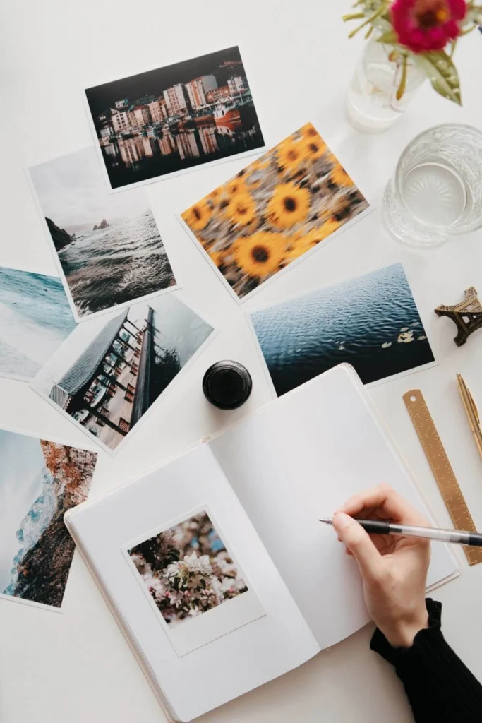 Flatlay of a travel journal surrounded by printed photos, sunflowers, and stationery for a creative travel scrapbook.