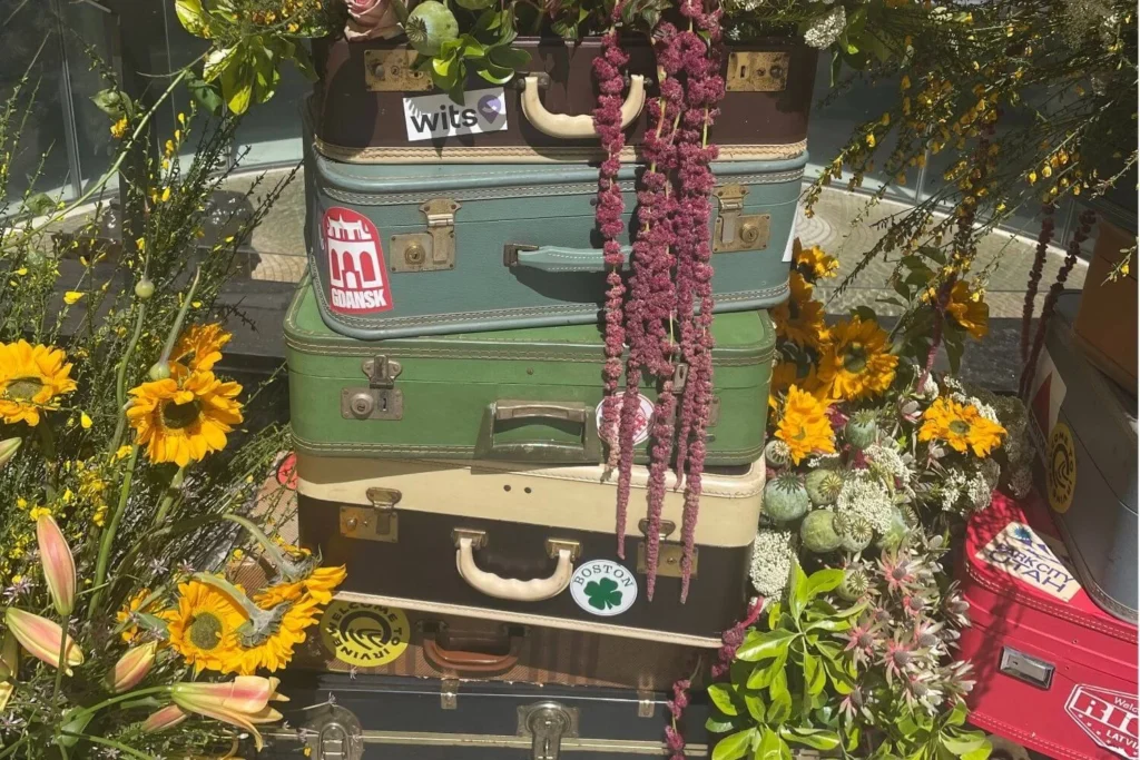 Vintage travel décor featuring a tall stack of colorful retro suitcases decorated with destination stickers and surrounded by bright sunflowers and lush greenery, perfect for inspiring wanderlust-themed home styling.