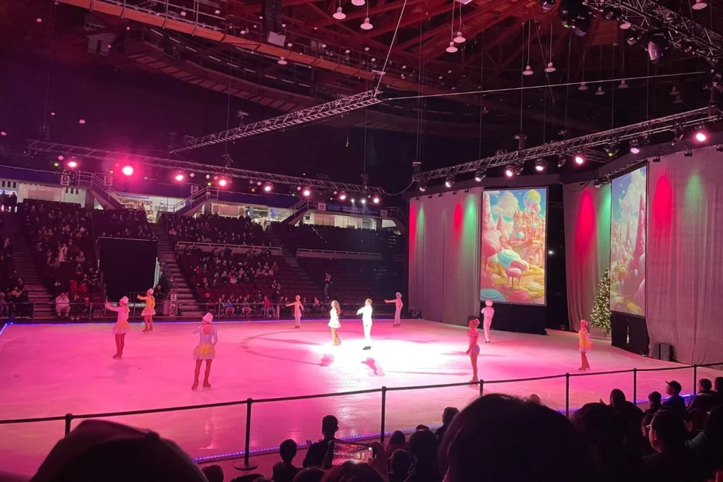 Ice skaters performing a colourful holiday show in a Vancouver arena with festive lighting and projected backdrops.