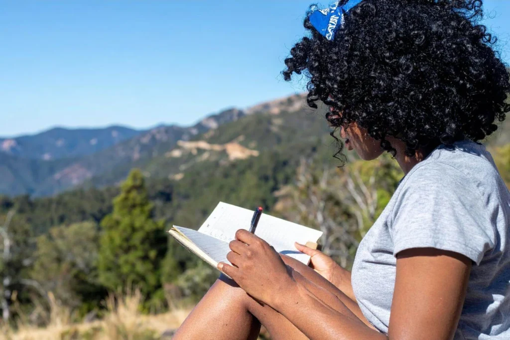 Solo female traveller journaling in nature with mountain views in the background.