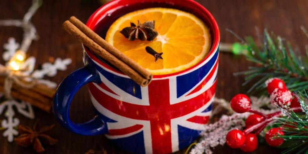 Union Jack mug filled with a warm British Christmas drink, garnished with orange and spices on a festive table.