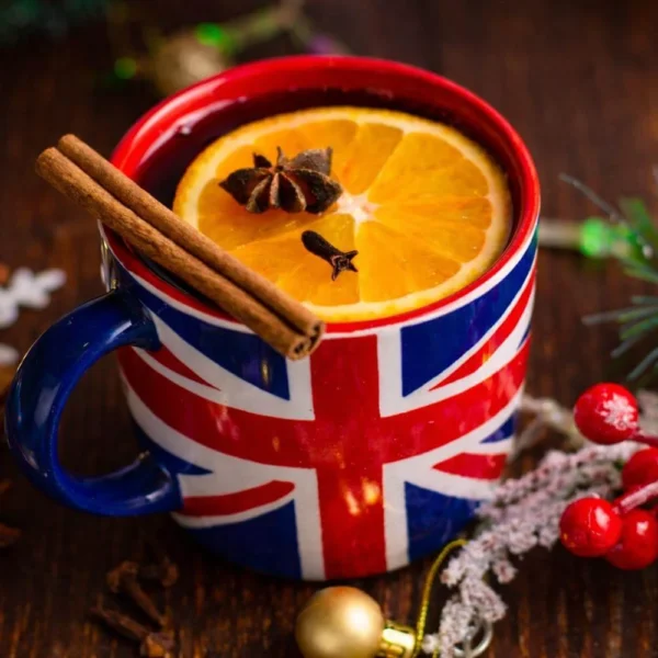 Union Jack mug filled with a warm British Christmas drink, garnished with orange and spices on a festive table.