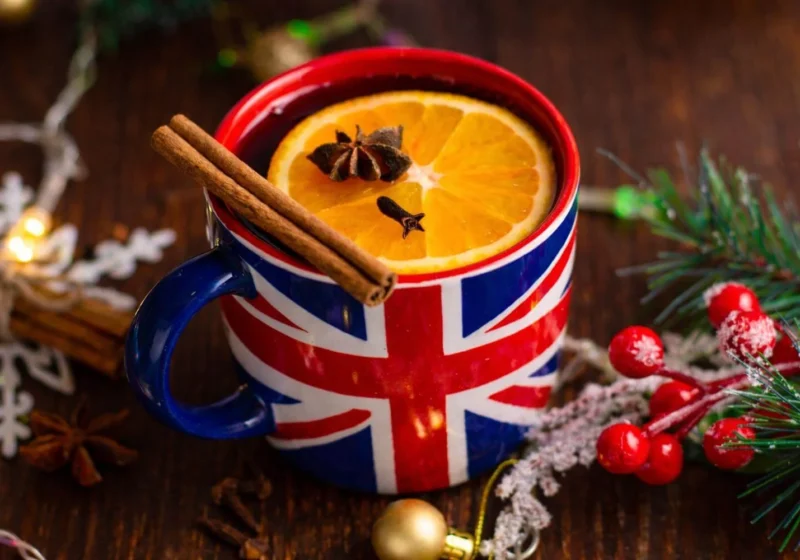 Union Jack mug filled with a warm British Christmas drink, garnished with orange and spices on a festive table.