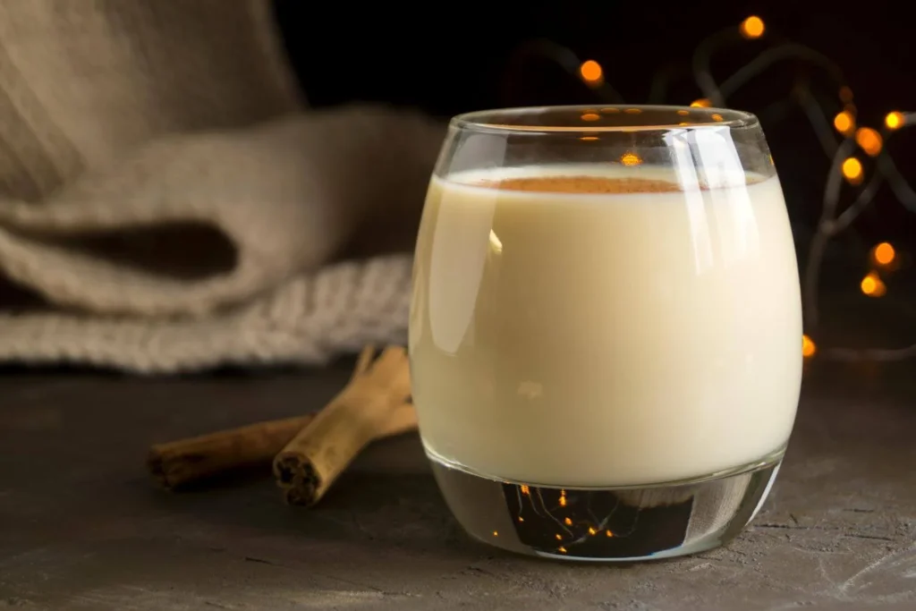 Glass of creamy British-style eggnog with cinnamon on top, styled for a cosy Christmas evening.