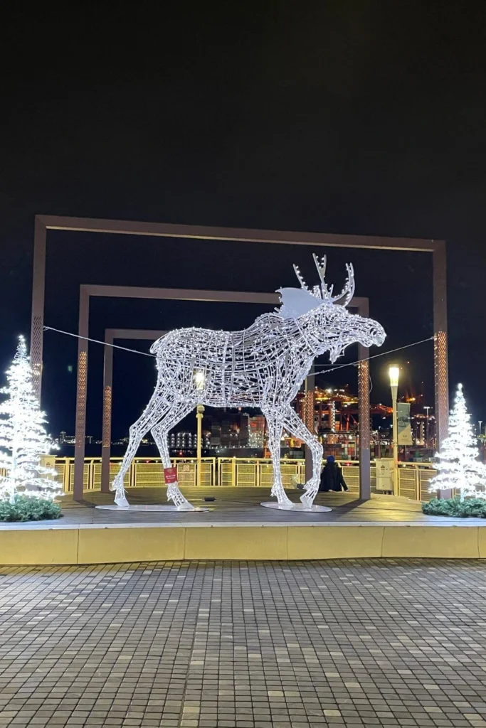 Large illuminated moose sculpture framed by glowing white Christmas trees and geometric arches at Canada Place in Vancouver.