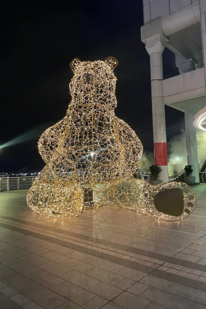 Massive seated bear sculpture made of golden Christmas lights on the outdoor promenade at Canada Place, glowing against the night sky.