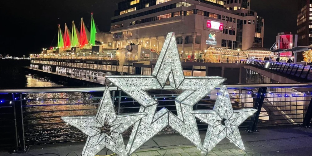 Three illuminated star sculptures on the Canada Place promenade, with sails of the convention center lit in red and green in the background for the holidays.