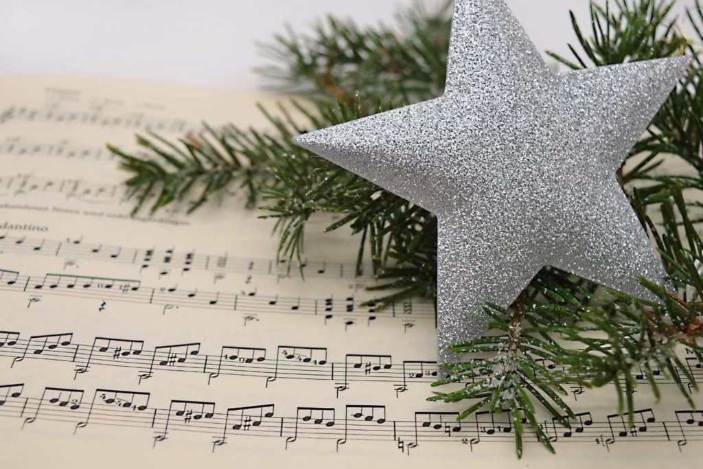 Close-up of a silver glitter star and pine branches resting on sheet music, evoking a festive, musical holiday theme.