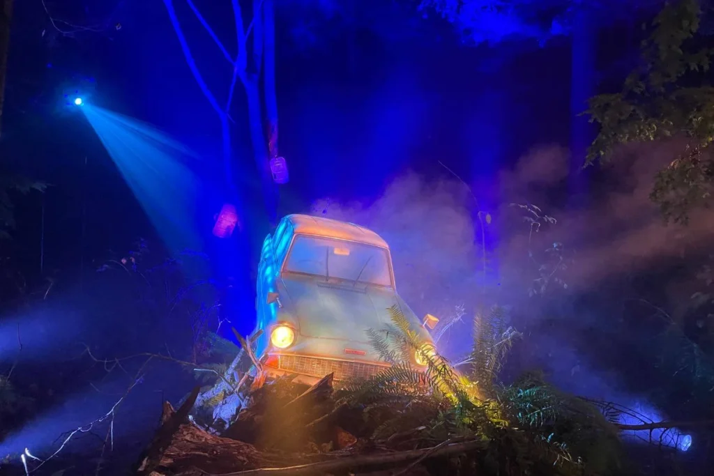 The iconic flying Ford Anglia crashed among branches and mist under dramatic blue lighting at the Harry Potter Forbidden Forest Experience.