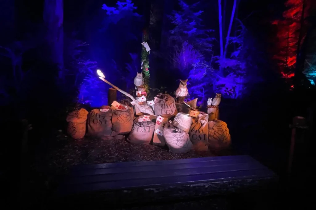 A magical Owl Post display with glowing owls, mailbags and Hogwarts letters set against blue-lit forest scenery at the Forbidden Forest Experience.