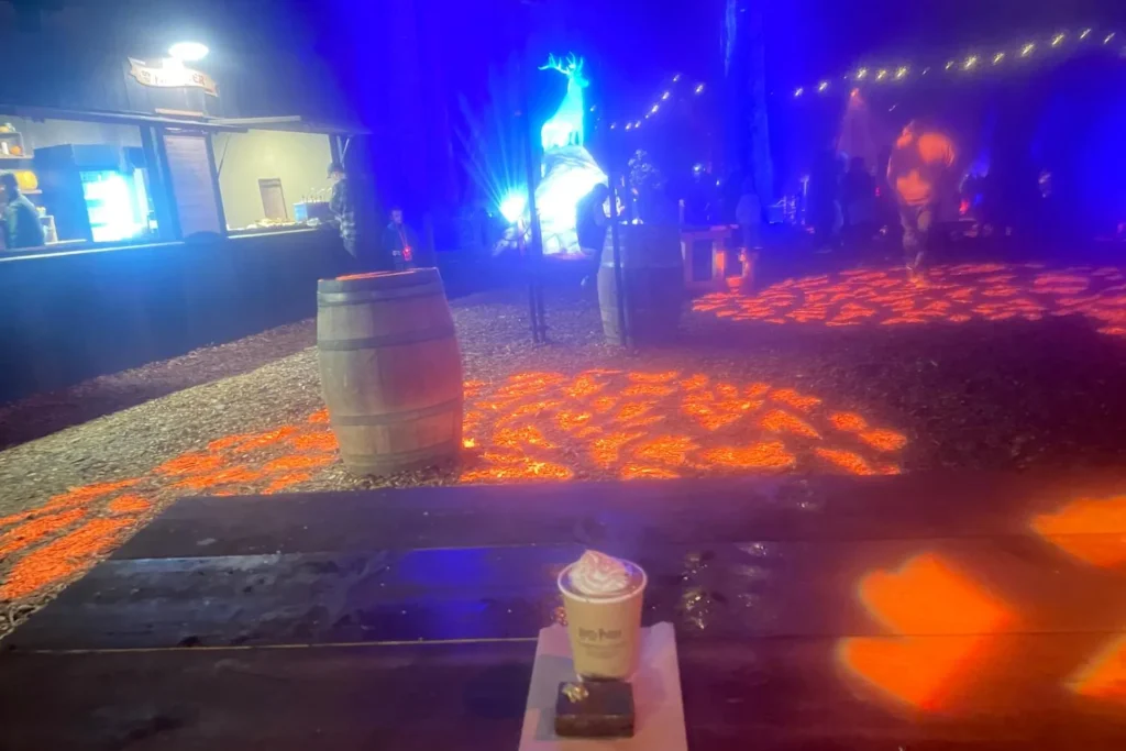 A table with hot chocolate and a brownie overlooking the glowing stag Patronus installation at the Harry Potter Forbidden Forest Experience.