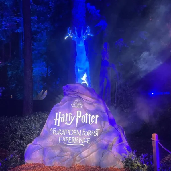 A glowing blue stag Patronus standing on a rock engraved with the Harry Potter Forbidden Forest Experience logo.
