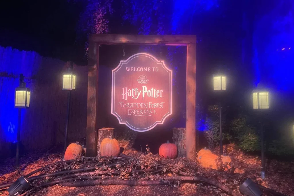 The illuminated welcome sign for the Harry Potter Forbidden Forest Experience displayed with pumpkins, branches and lanterns.