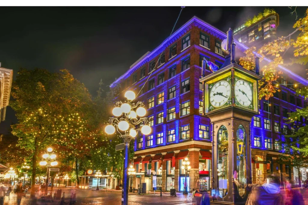 Gastown steam clock area in Vancouver at night, with festive lights on the building and street.