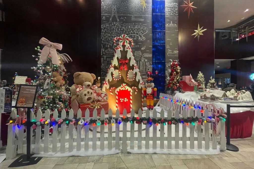 Indoor Christmas display featuring a giant gingerbread house, teddy bears, Christmas trees, and festive decorations inside a Vancouver hotel lobby.