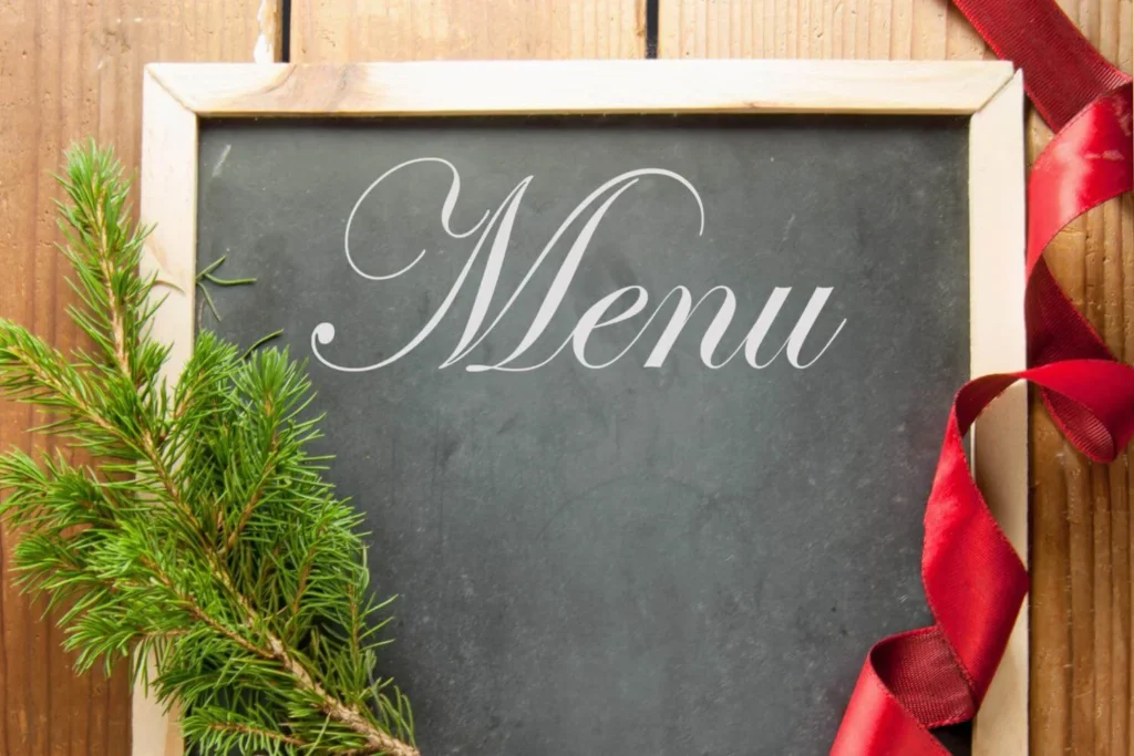 Blank chalkboard labeled “Menu” framed in wood, with a red satin ribbon and pine sprig for a festive touch, ideal for holiday meal planning.