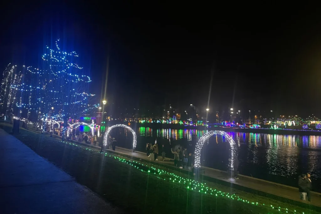 White light arches and illuminated trees lining the waterfront path at Lafarge Lake in Coquitlam, with colourful reflections shimmering across the water during the Lights at Lafarge display.