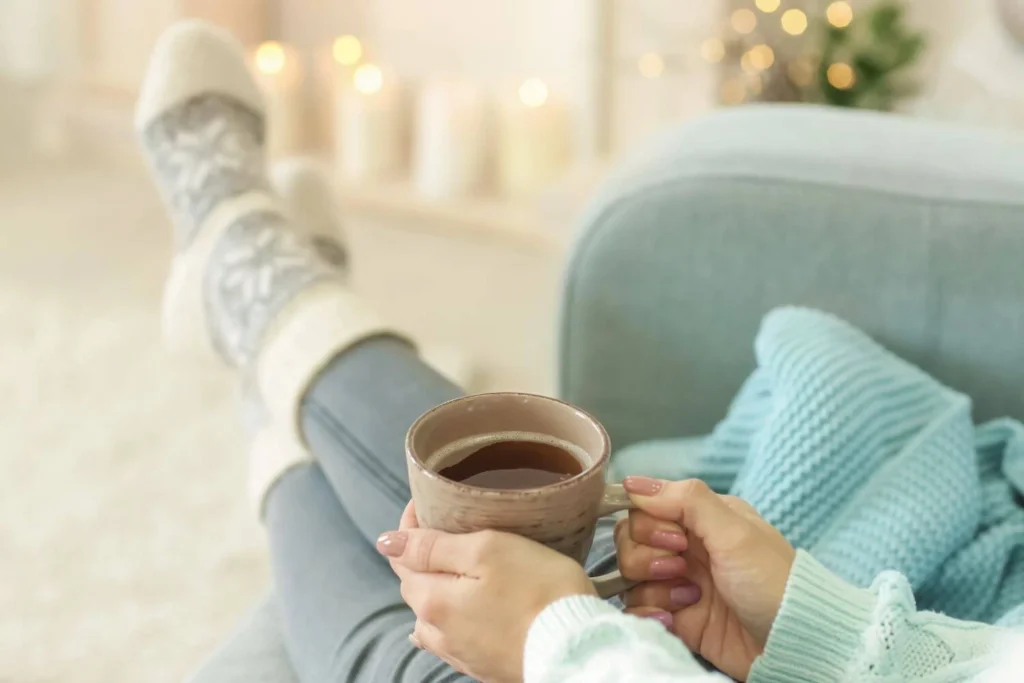 Person relaxing at home with a hot drink, representing rest and self-care while recovering from political burnout.