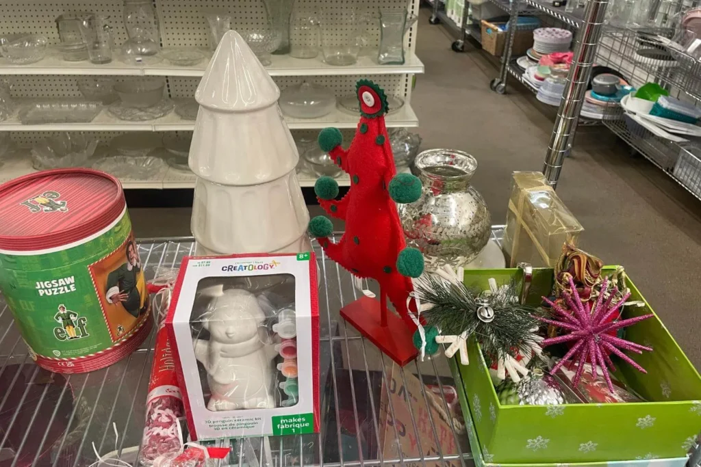 Eclectic mix of thrifted Christmas items including a ceramic tree, felt decor, Elf jigsaw puzzle, and a paint-your-own penguin kit.