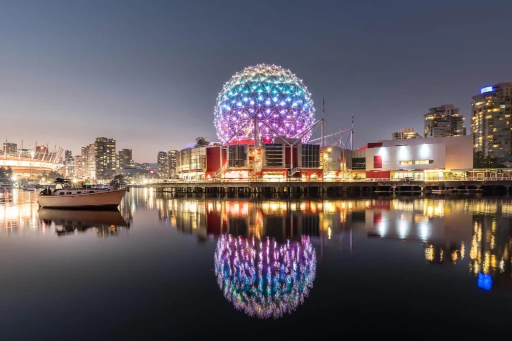 Science World lit up with colorful Christmas lights reflected on the water in Vancouver at night.