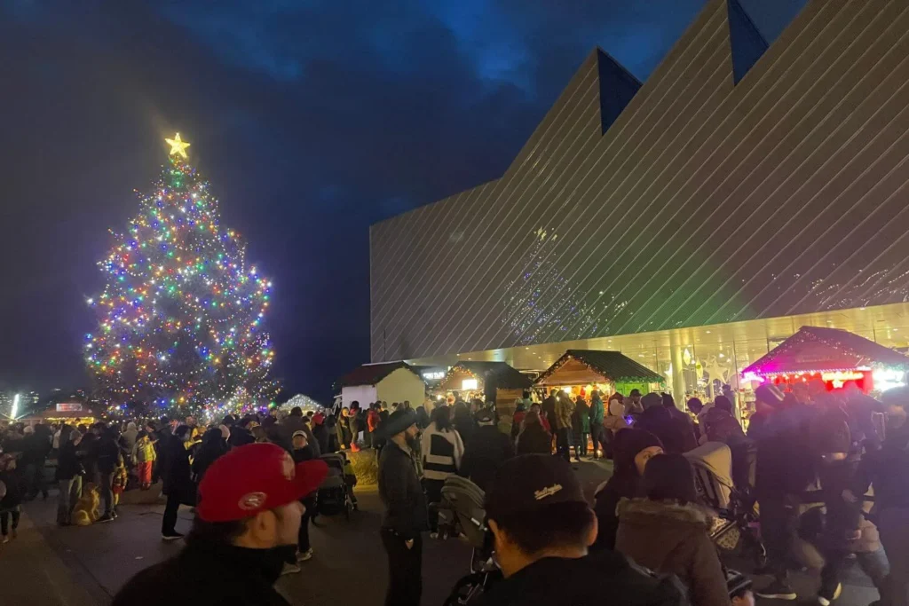 Large decorated Christmas tree and festive market stalls at the Shipyards Christmas Market in North Vancouver, with crowds enjoying the holiday lights at night.