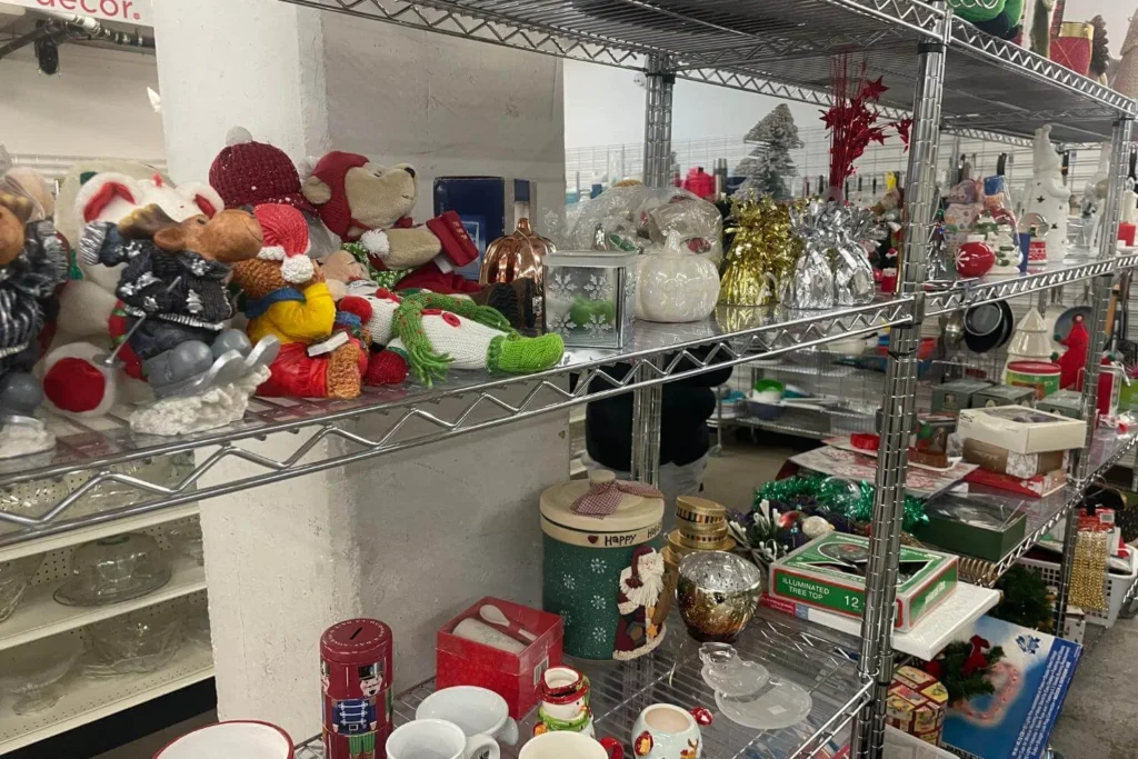 Shelves filled with secondhand Christmas decorations at a thrift store, including plush toys, ornaments, candles, and festive trinkets.