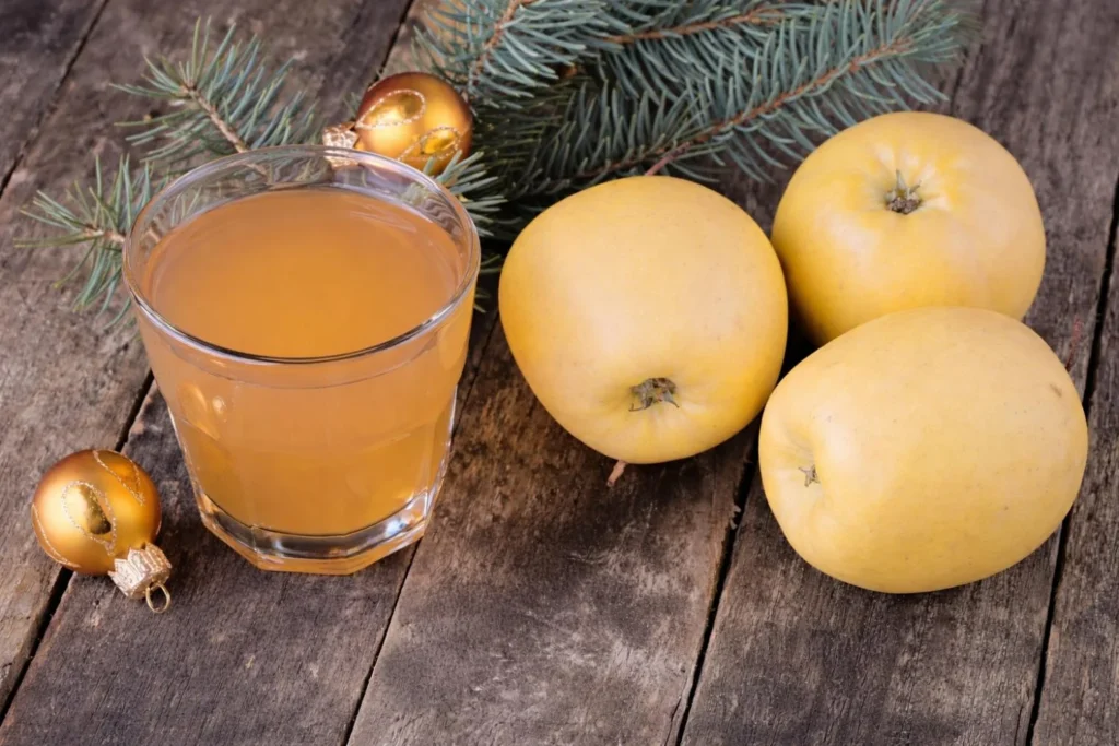 Glass of toffee apple cider with fresh apples on a rustic table.