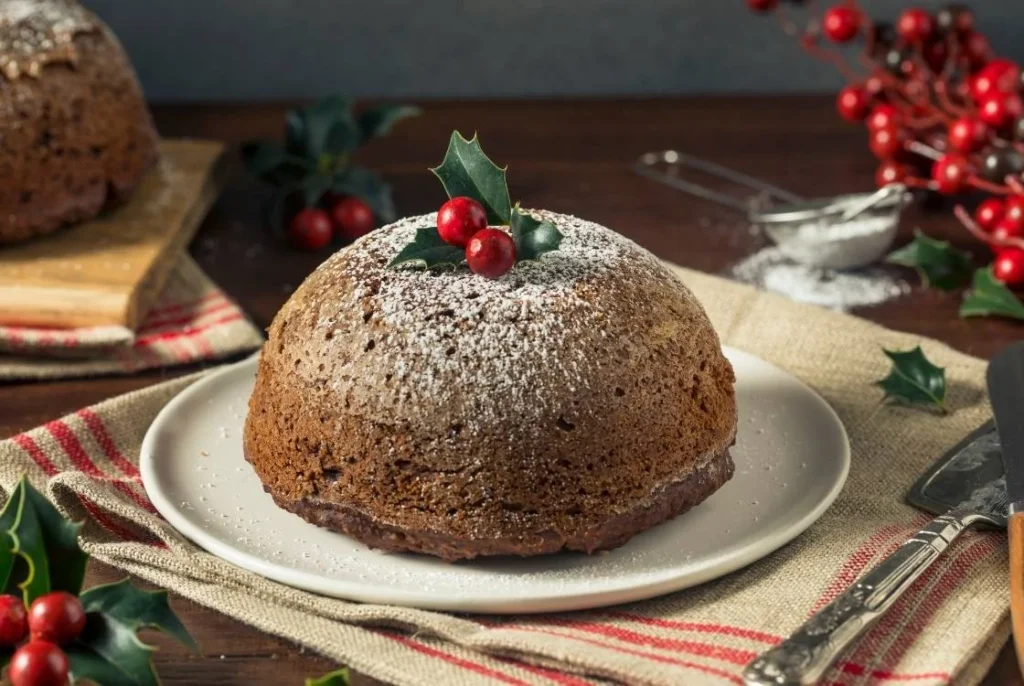 Traditional British figgy pudding dusted with icing sugar and topped with holly, served as a classic Christmas dessert.