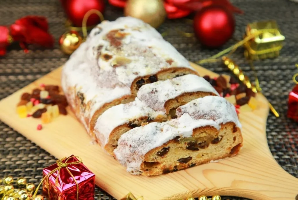 Traditional German stollen dusted with powdered sugar, sliced to show dried fruit and marzipan, served as a classic Christmas dessert.
