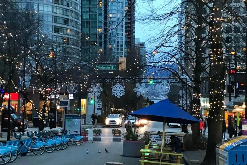 Robson Street in Vancouver at Christmas with festive lights, city buildings, and pedestrians in the early evening.