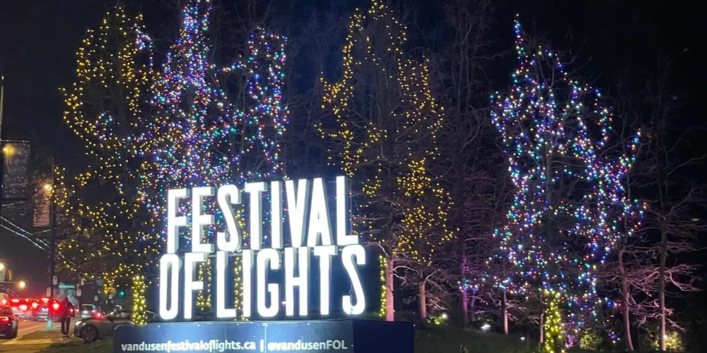 Festival of Lights entrance sign at VanDusen Botanical Garden in Vancouver, with colorful Christmas lights wrapped around bare trees at night.