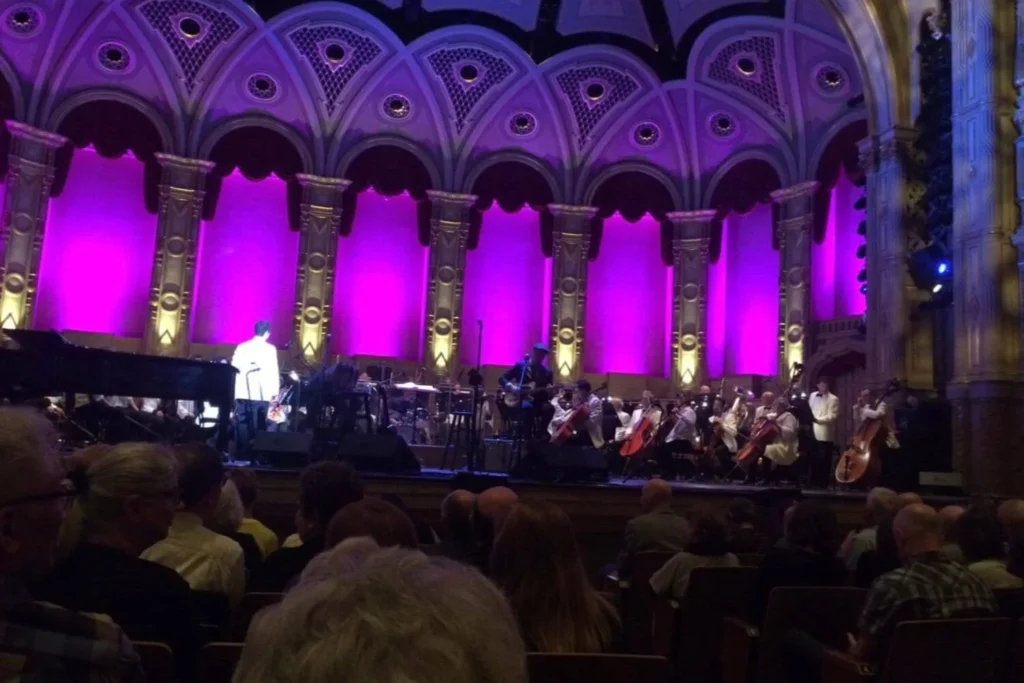View of the Vancouver Symphony Orchestra performing West Side Story at the Orpheum Theatre, with musicians on stage and purple lighting highlighting the venue’s ornate arches.