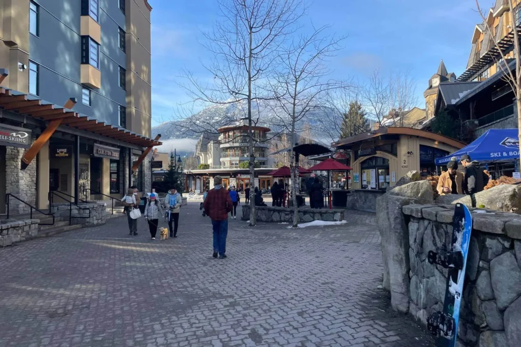 Whistler Village in December with snow on the ground, mountain views, and people walking through the village.