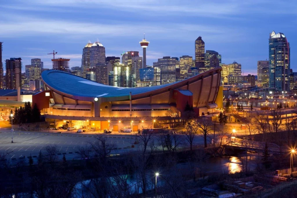 Calgary skyline at night featuring the Scotiabank Saddledome and downtown buildings.