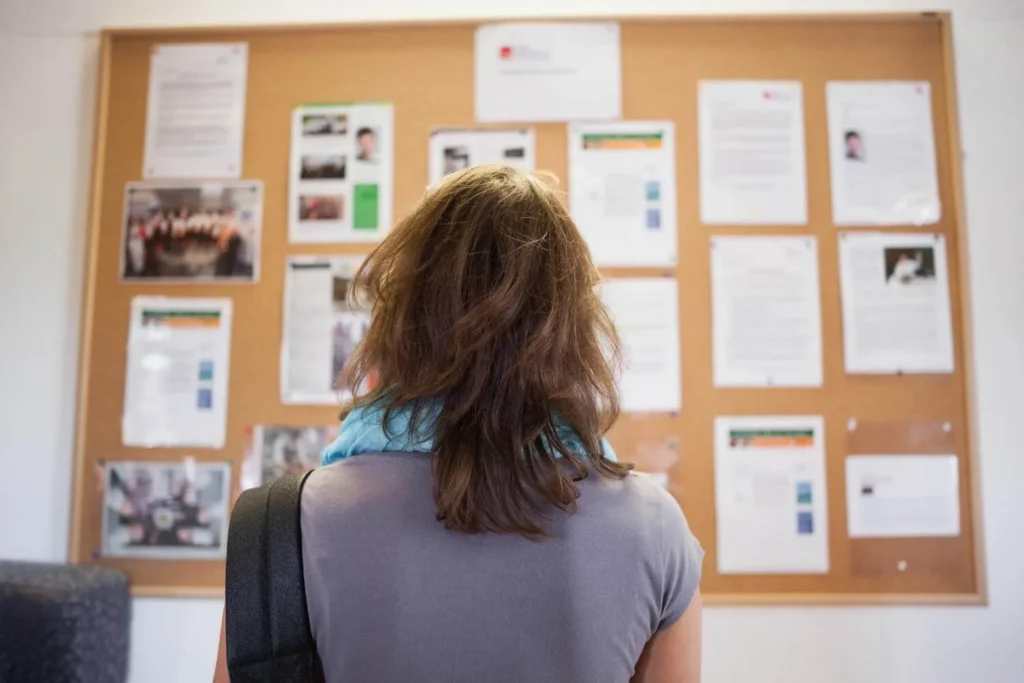 Person standing in front of a public notice board reading posted announcements and community information.