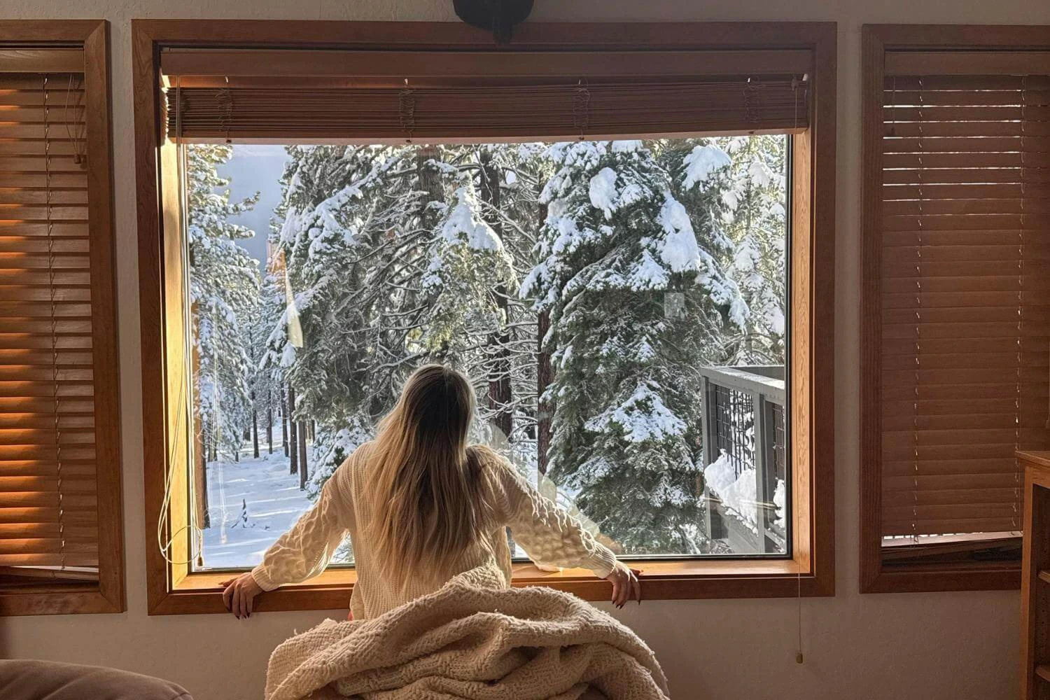 Solo traveler spending winter alone at home, looking out at snowy trees and reflecting quietly.