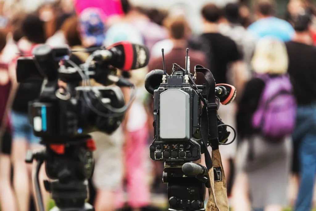Professional video camera recording a large crowd at a public gathering.