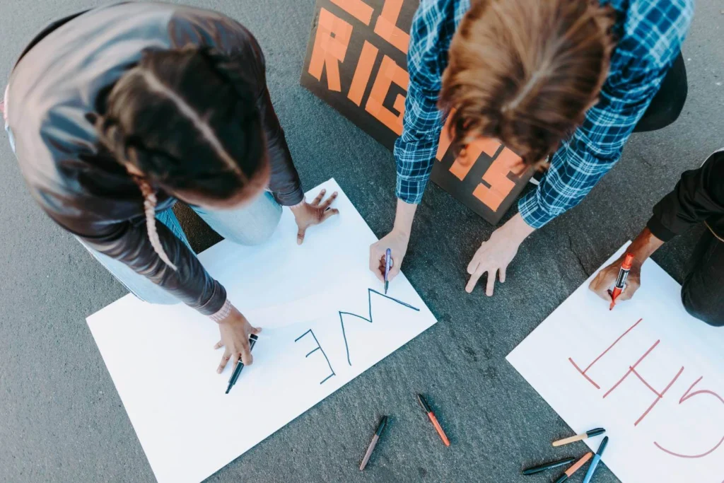 Group of people creating handmade signs together on the ground using markers.