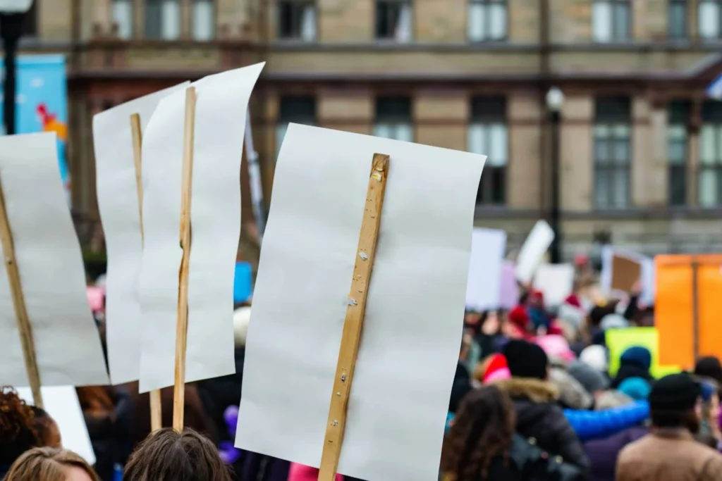 Large crowd holding signs during a public demonstration in an urban setting.
