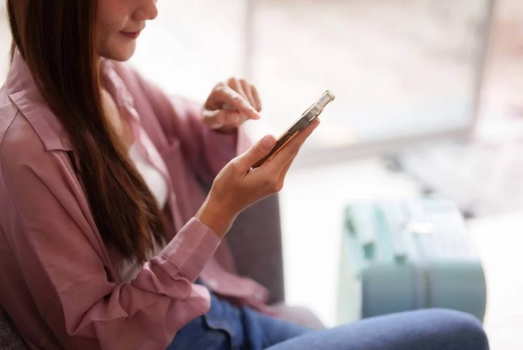 Solo female traveler checking her phone while sitting next to a suitcase before a trip.