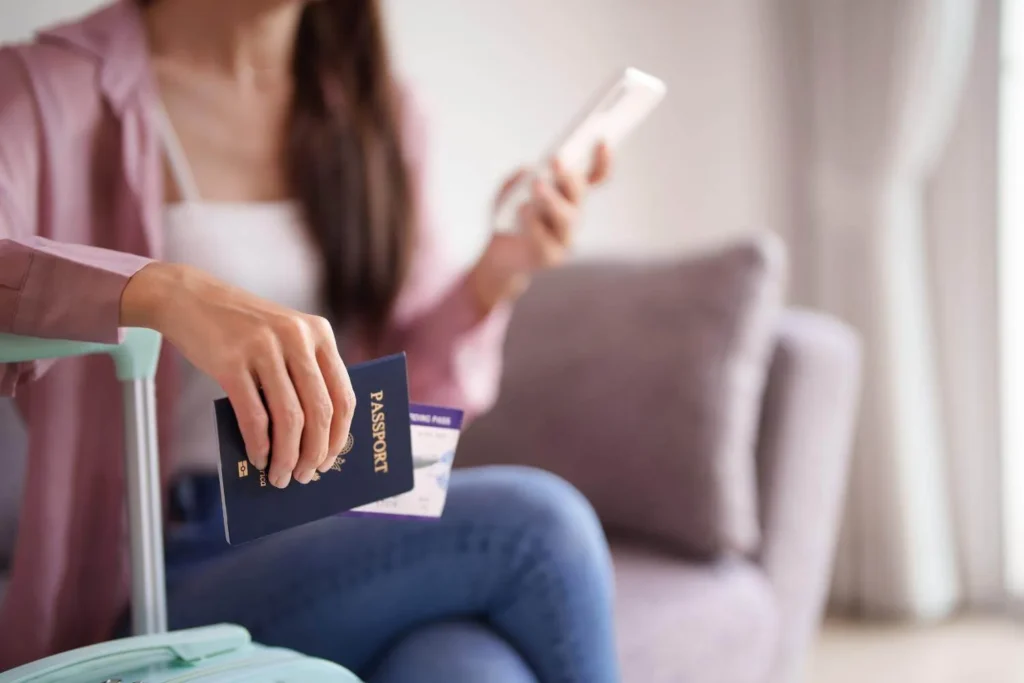 Solo female traveler holding a passport and phone while sitting next to a suitcase, preparing for a solo trip.