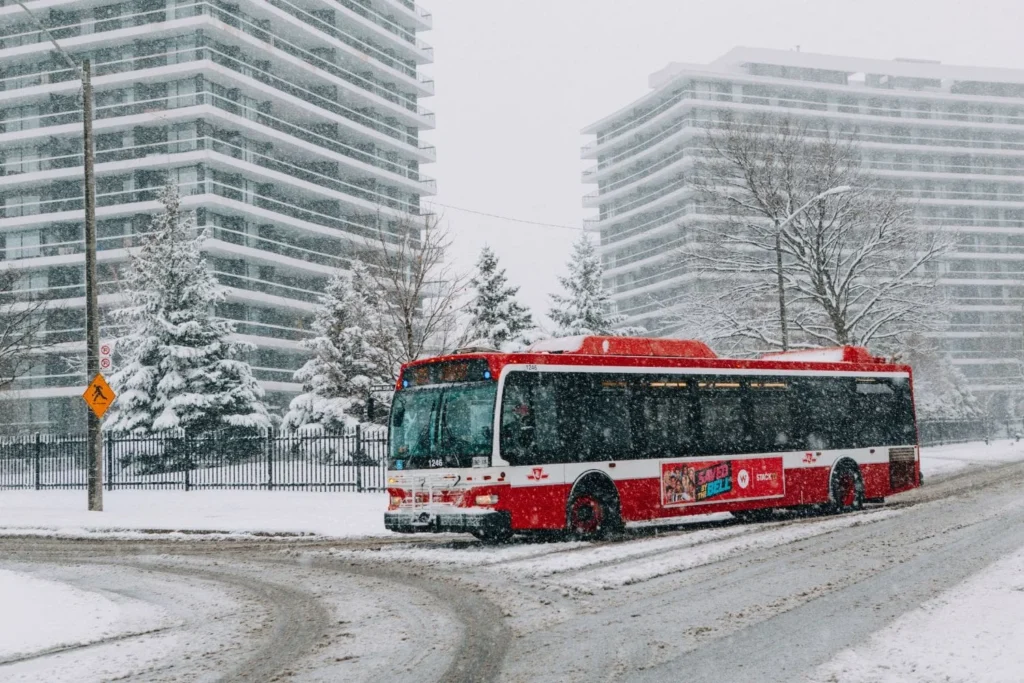 Red Toronto public transit bus driving through heavy snow during winter, showing real winter travel conditions in Canada.