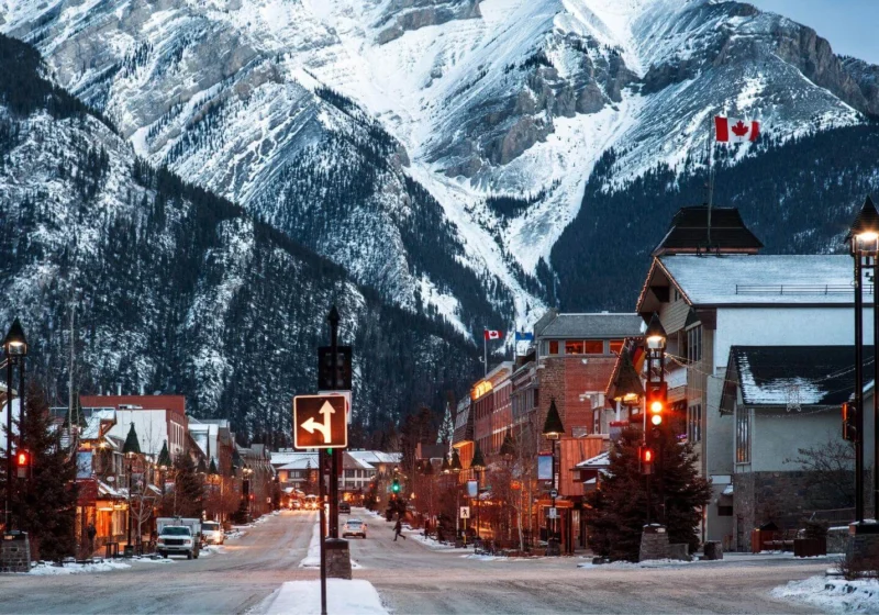 Winter street scene in Banff, Canada with snow-covered mountains and town lights, showing what winter travel in Canada looks like for solo travelers.