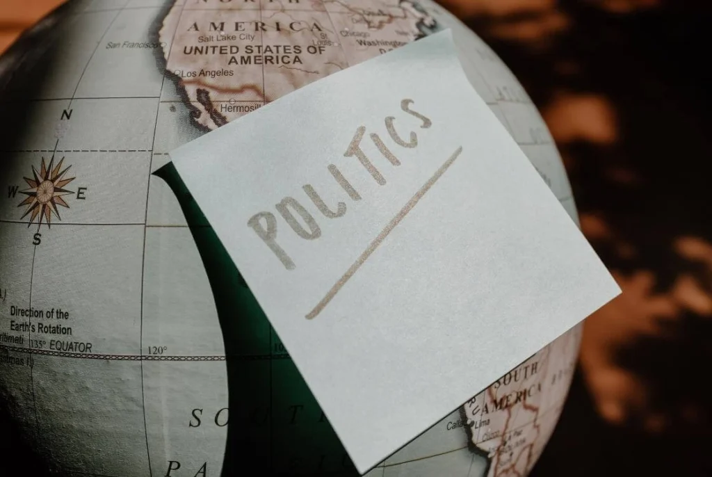 White card with the word "POLITICS" resting on a globe showing North and South America illustrating how political issues and decisions are connected to travel opportunities, experiences, and life around the world.